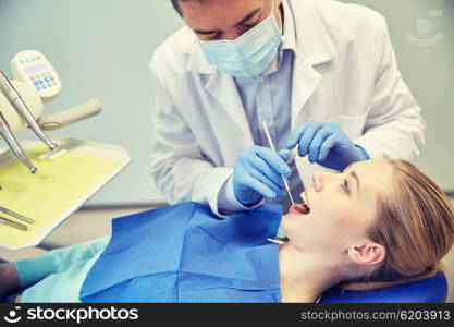 people, medicine, stomatology and health care concept - male dentist in mask with dental mirror and probe checking female patient teeth up at dental clinic office