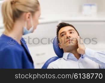 people, medicine, stomatology and health care concept - male patient with toothache complaining to female dentist at dental clinic office