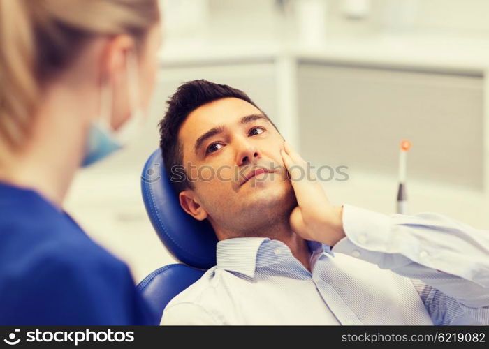 people, medicine, stomatology and health care concept - male patient with toothache complaining to female dentist at dental clinic office