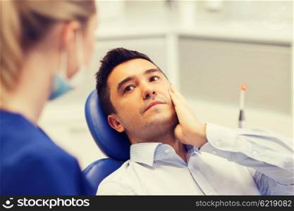 people, medicine, stomatology and health care concept - male patient with toothache complaining to female dentist at dental clinic office