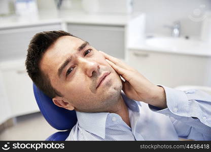 people, medicine, stomatology and health care concept - unhappy male patient having toothache sitting on dental chair at clinic office