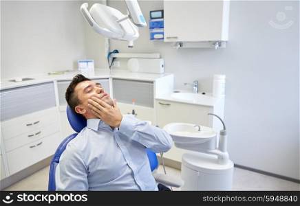 people, medicine, stomatology and health care concept - unhappy male patient having toothache sitting on dental chair at clinic office