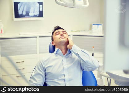 people, medicine, stomatology and health care concept - unhappy male patient having toothache sitting on dental chair at clinic office