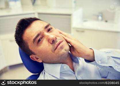 people, medicine, stomatology and health care concept - unhappy male patient having toothache sitting on dental chair at clinic office