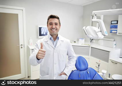 people, medicine, stomatology and healthcare concept - happy middle aged male dentist in white coat showing thumbs up at dental clinic office