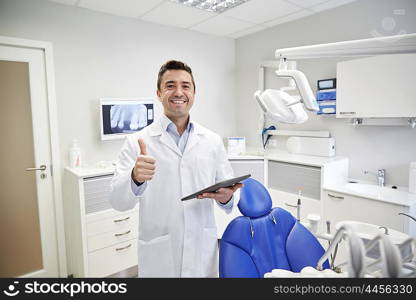 people, medicine, stomatology and healthcare concept - happy middle aged male dentist in white coat with tablet pc computer showing thumbs up at dental clinic office