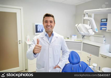 people, medicine, stomatology and healthcare concept - happy middle aged male dentist in white coat showing thumbs up at dental clinic office