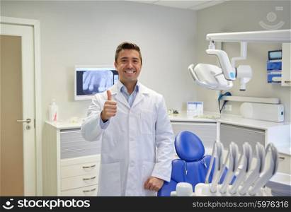 people, medicine, stomatology and healthcare concept - happy middle aged male dentist in white coat showing thumbs up at dental clinic office