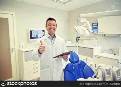 people, medicine, stomatology and healthcare concept - happy middle aged male dentist in white coat with tablet pc computer showing thumbs up at dental clinic office