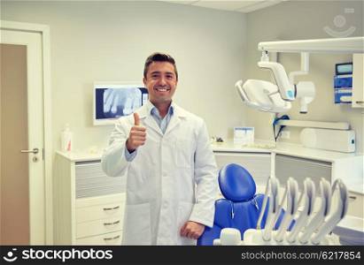 people, medicine, stomatology and healthcare concept - happy middle aged male dentist in white coat showing thumbs up at dental clinic office