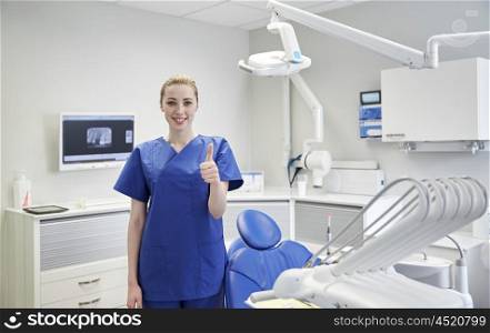 people, medicine, stomatology and healthcare concept - happy young female dentist showing thumbs up at dental clinic office
