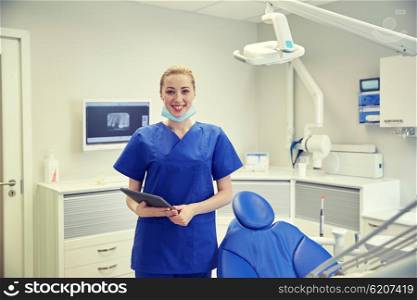 people, medicine, stomatology and healthcare concept - happy young female dentist with tablet pc computer at dental clinic office