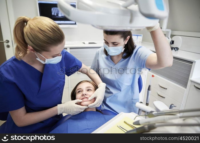 people, medicine, stomatology and teeth care concept - happy female dentist with assistant checking patient girl dental occlusion teeth at dental clinic office