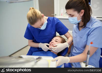 people, medicine, stomatology and teeth care concept - happy female dentist with assistant checking patient girl dental occlusion teeth at dental clinic office