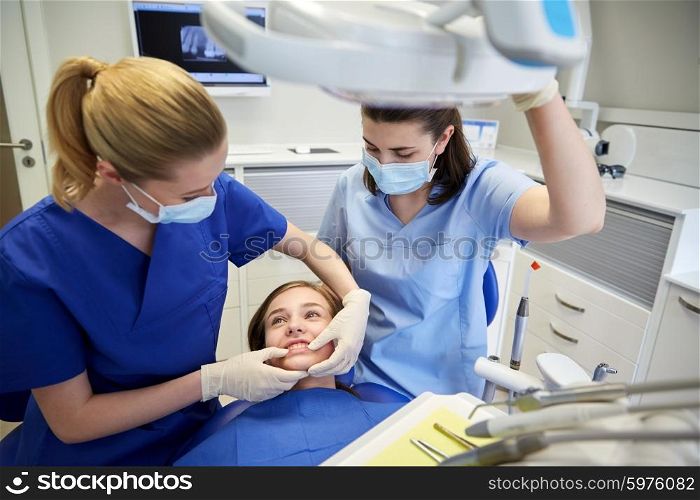 people, medicine, stomatology and teeth care concept - happy female dentist with assistant checking patient girl dental occlusion teeth at dental clinic office