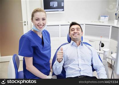 people, medicine, stomatology, gesture and health care concept - happy female dentist with man patient showing thumbs up at dental clinic office