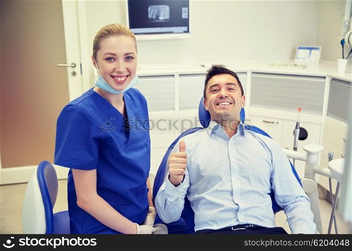 people, medicine, stomatology, gesture and health care concept - happy female dentist with man patient showing thumbs up at dental clinic office