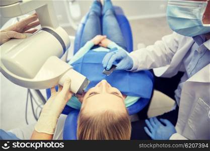 people, medicine, stomatology, technology and health care concept - close up of dentist putting intraoral shield to female patient mouth and assistant directing x-ray machine at dental clinic