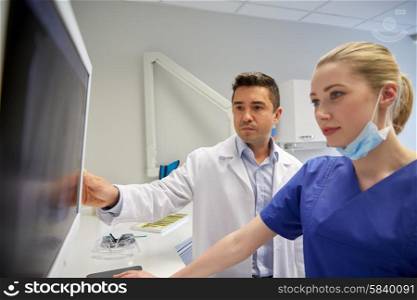 people, medicine, stomatology, technology and health care concept - dentists looking to x-ray scan on monitor at dental clinic