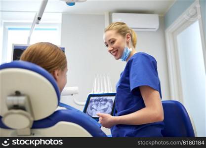 people, medicine, stomatology, technology and health care concept - happy female dentist showing teeth x-ray on tablet pc computer to patient girl at dental clinic office