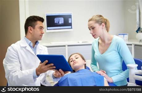 people, medicine, stomatology, technology and health care concept - male dentist showing tablet pc computer to patient girl and her mother at dental clinic office