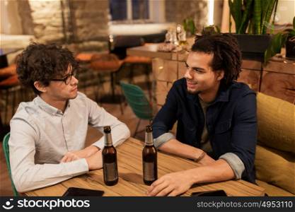 people, men, leisure, friendship and communication concept - happy male friends drinking bottled beer and talking at bar or pub. happy male friends drinking beer at bar or pub