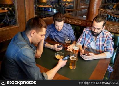 people, men, leisure, friendship and communication concept - male friends with smartphones drinking draft beer at bar or pub