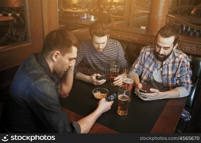 people, men, leisure, friendship and communication concept - male friends with smartphones drinking draft beer at bar or pub