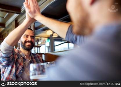 people, men, leisure, friendship and gesture concept - happy male friends drinking draft beer and making high five at bar or pub