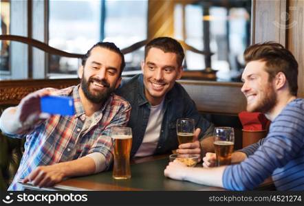 people, men, leisure, friendship and technology concept - happy male friends drinking beer and taking selfie with smartphone at bar or pub