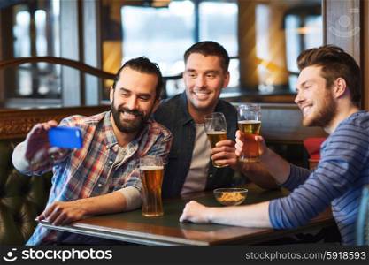 people, men, leisure, friendship and technology concept - happy male friends drinking beer and taking selfie with smartphone at bar or pub