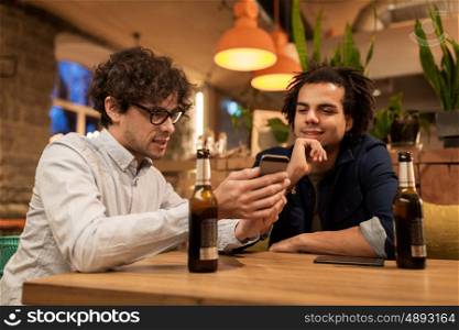 people, men, leisure, friendship and technology concept - happy male friends with smartphones drinking bottled beer at bar or pub