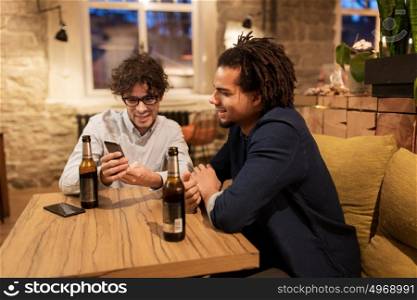 people, men, leisure, friendship and technology concept - happy male friends with smartphones drinking bottled beer at bar or pub. men with smartphones drinking beer at bar or pub