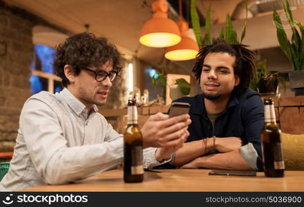 people, men, leisure, friendship and technology concept - happy male friends with smartphones drinking bottled beer at bar or pub. men with smartphones drinking beer at bar or pub