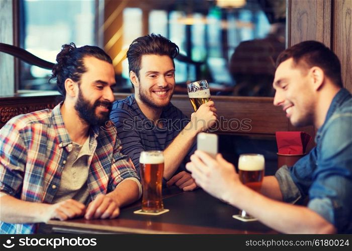 people, men, leisure, friendship and technology concept - happy male friends with smartphone drinking beer at bar or pub