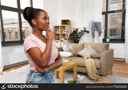 people, mess and cleaning concept - happy african american young woman thinking over dirty room background. african american woman thinking over dirty room