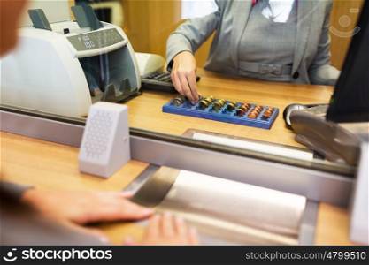 people, money, saving and finance concept - clerk counting coins for customer at bank office or currency exchanger