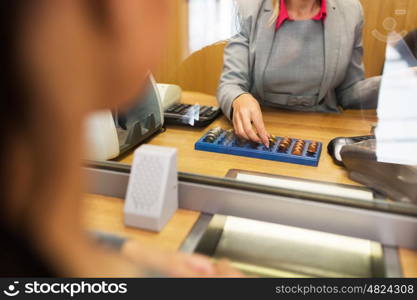 people, money, saving and finance concept - clerk counting coins for customer at bank office or currency exchanger