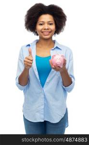 people, money saving and finances concept - happy african american young woman with piggy bank showing thumbs up over white