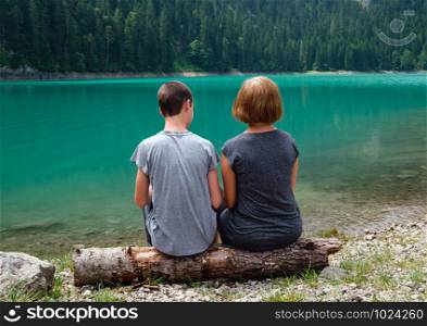 People, mother with son, rest on tree log on Black lake, Crno jezero, shore, summer landscape. Zabljak Municipality, Montenegro.