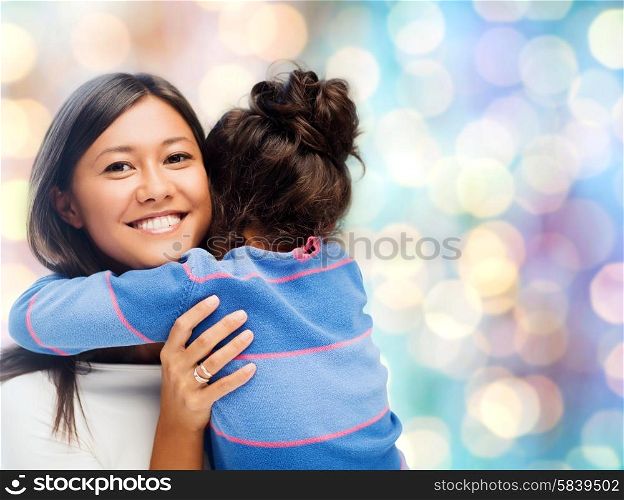 people, motherhood, family and adoption concept - happy mother and daughter hugging over blue holidays lights background