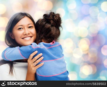 people, motherhood, family and adoption concept - happy mother and daughter hugging over blue holidays lights background