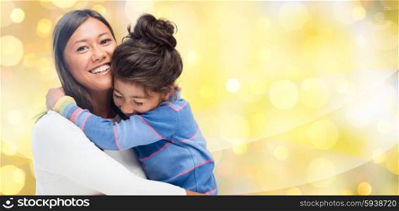 people, motherhood, family, holidays and adoption concept - happy mother and daughter hugging over yellow lights background
