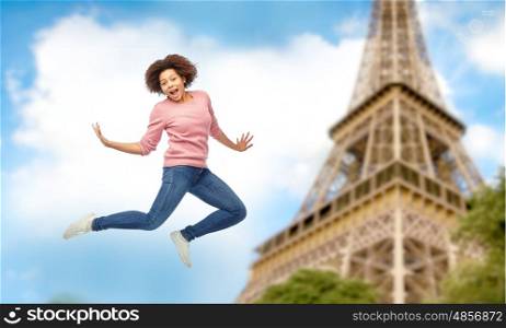 people, motion and action concept - happy african american young woman jumping over paris eiffel tower background