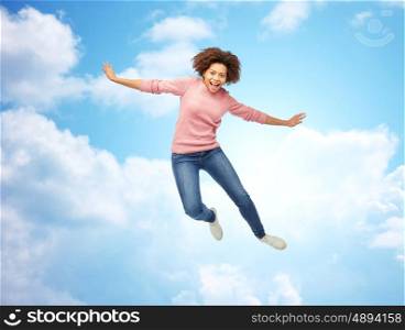 people, motion and action concept - happy african american young woman jumping over blue sky and clouds background
