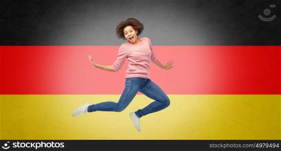 people, motion and action concept - happy african american young woman jumping over german flag background. african american woman jumping over german flag