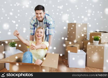 people, moving and real estate concept - happy couple having fun and riding in cardboard boxes at new home over snow