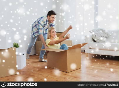 people, moving and real estate concept - happy couple having fun and riding in cardboard boxes at new home over snow