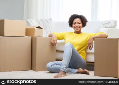 people, moving new place and repair concept - happy african american young woman with many cardboard boxes sitting on floor at home