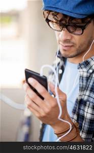 people, music, technology, leisure and lifestyle - close up of young hipster man with earphones and smartphone listening to music